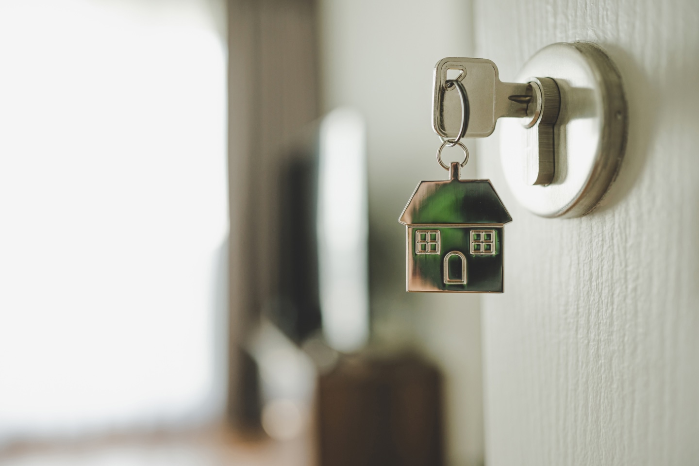 Key in keyhole of white door with small house shaped keychain