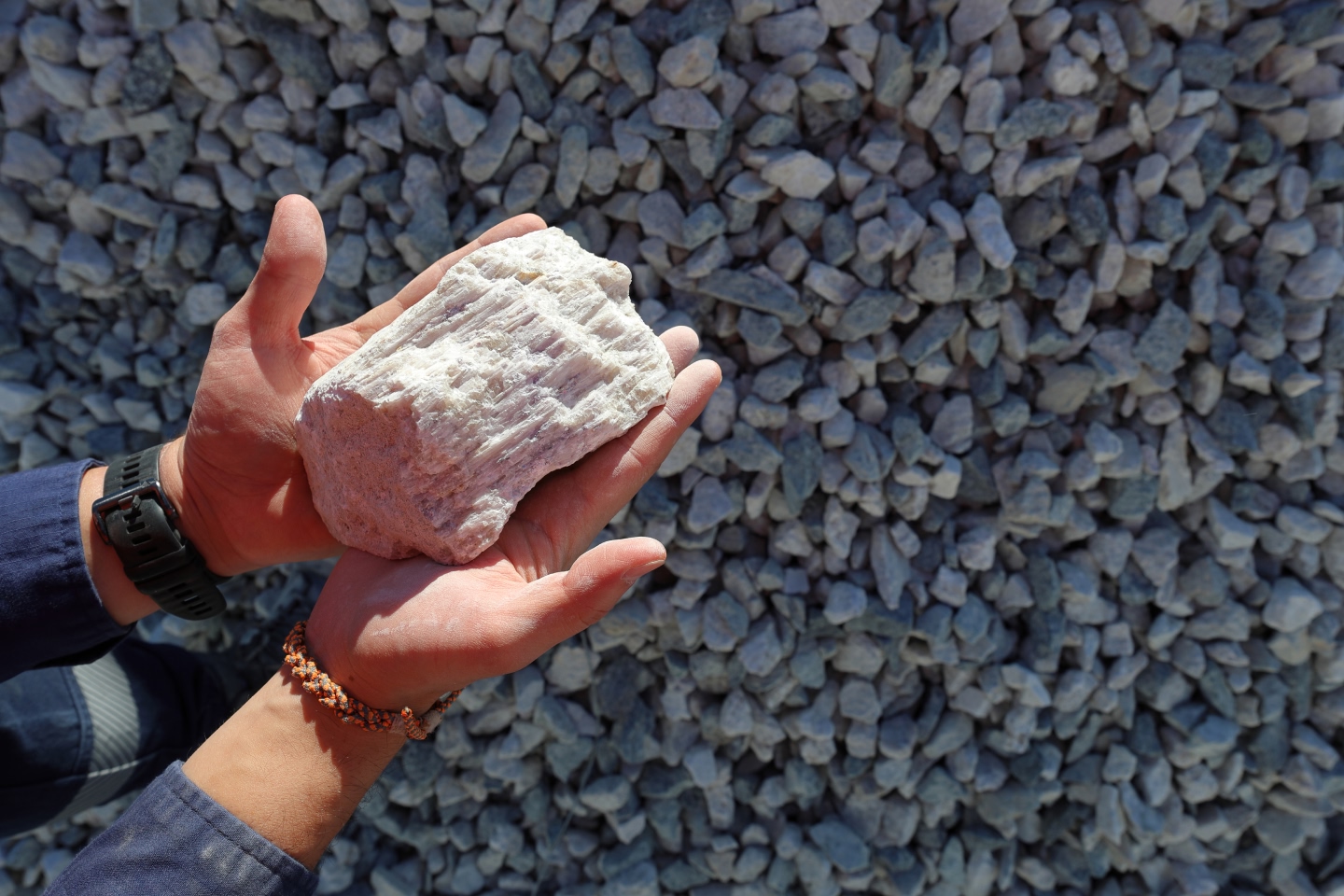 Person holding lithium ore in their hands over pebbles