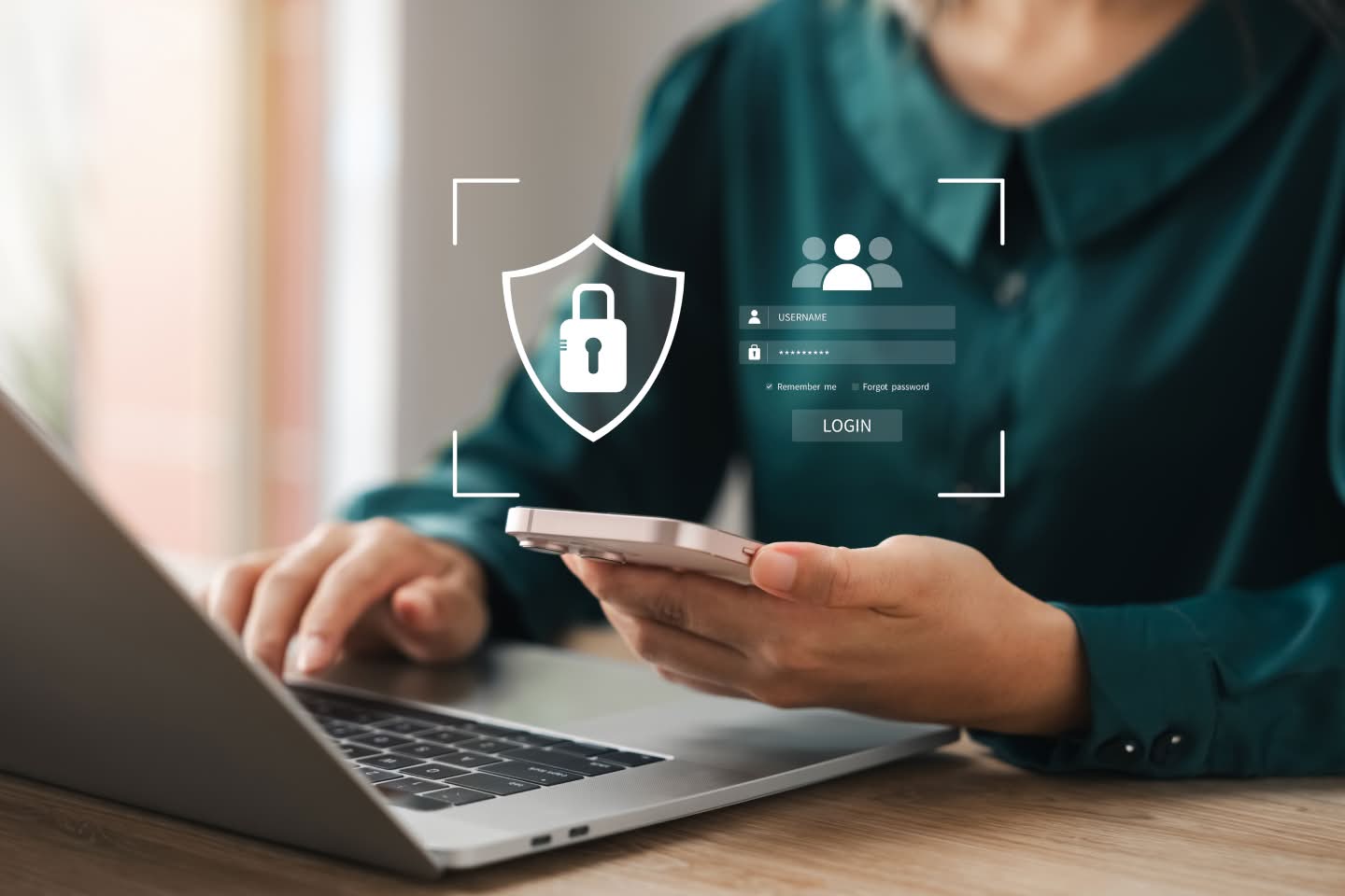 A person in a teal jumper with one hand using their laptop and the other on their phone, overlaid by a transparent security popup