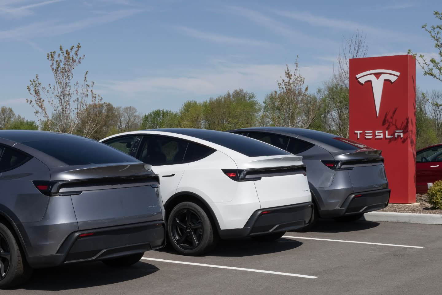 Three electric Tesla vehicles parked in front of a Tesla sign
