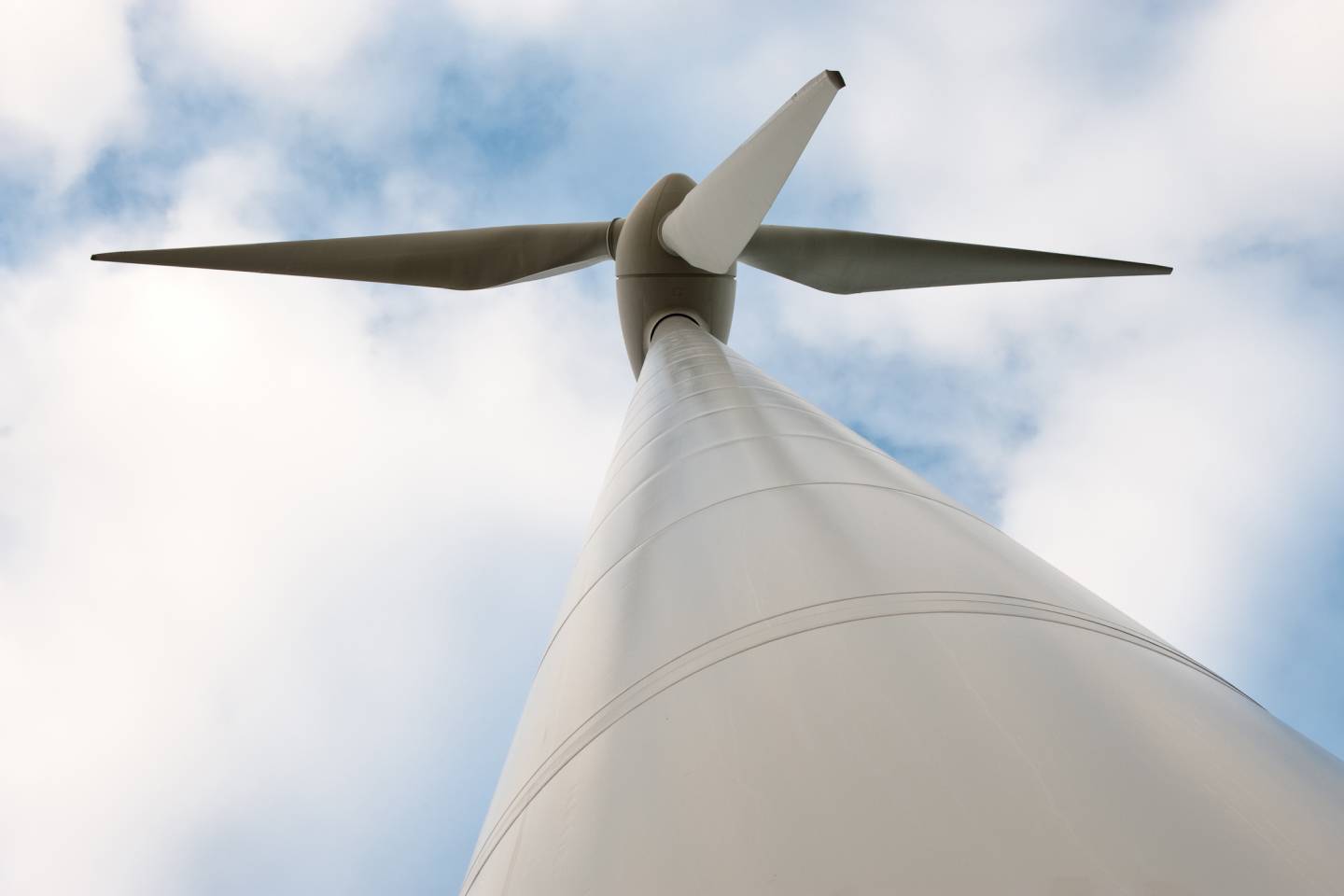 A large, modern wind turbine viewed from its base, showing the central hub and two propeller blades against the sky.