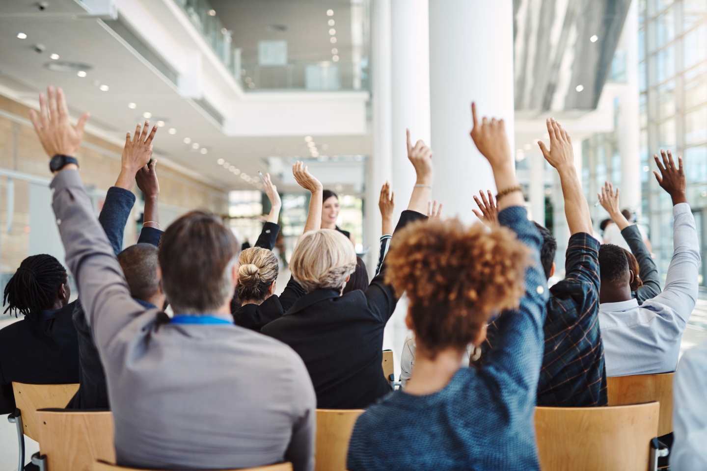 Room full of people at a business raising their hands, asking questions
