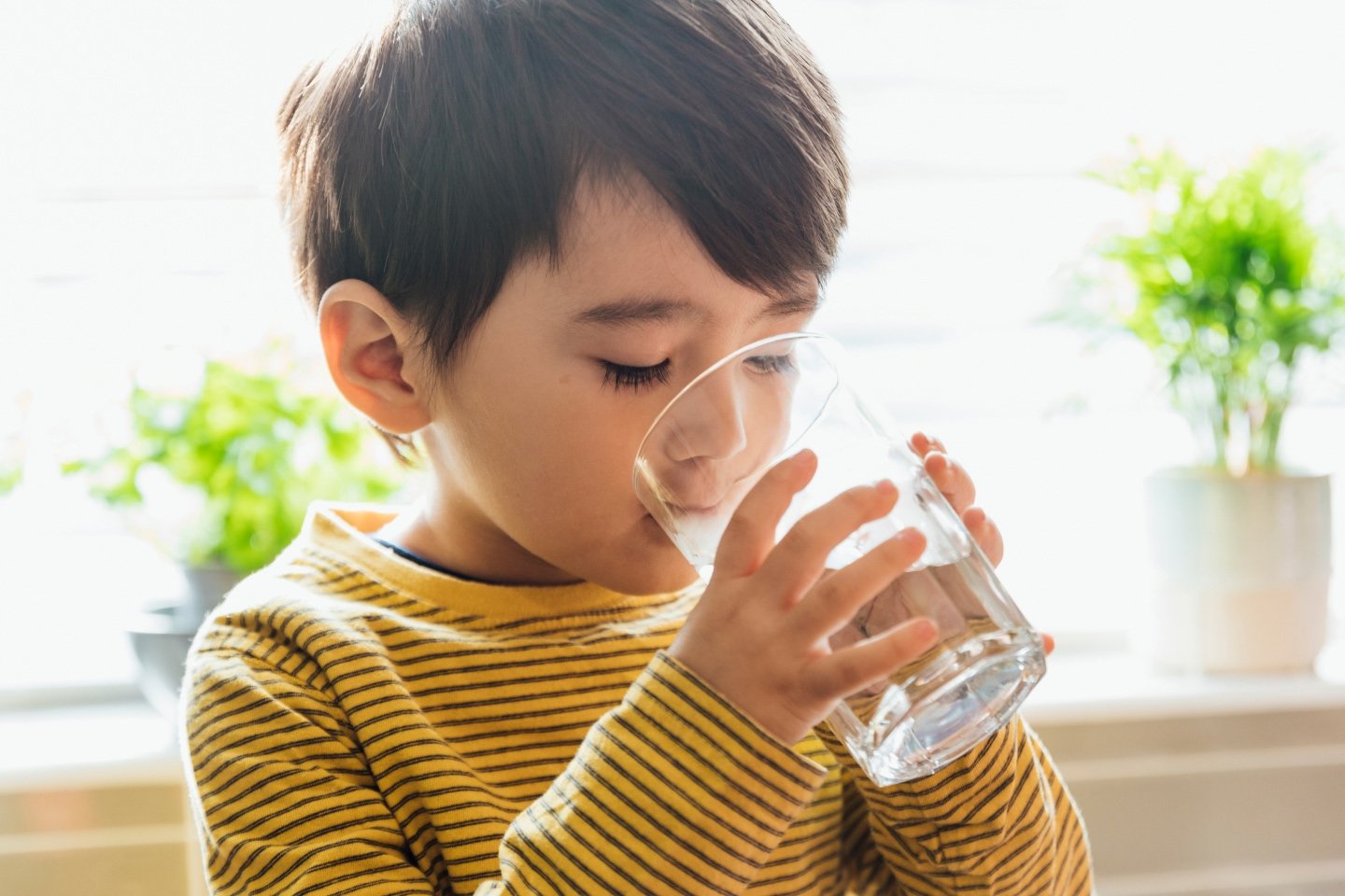 Child in a striped yellow top drinking water from a glass