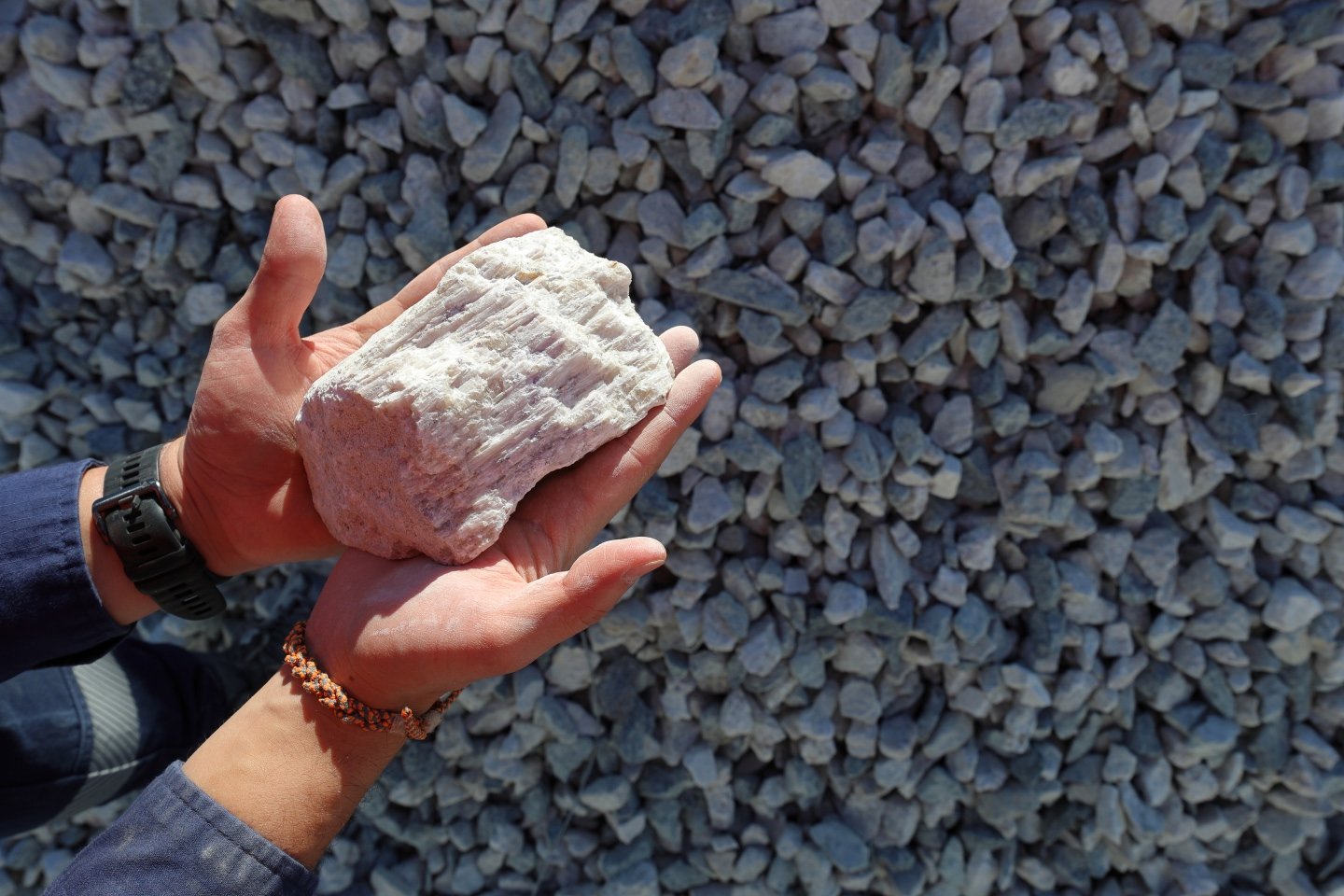 Person holding lithium ore in their hands over pebbles