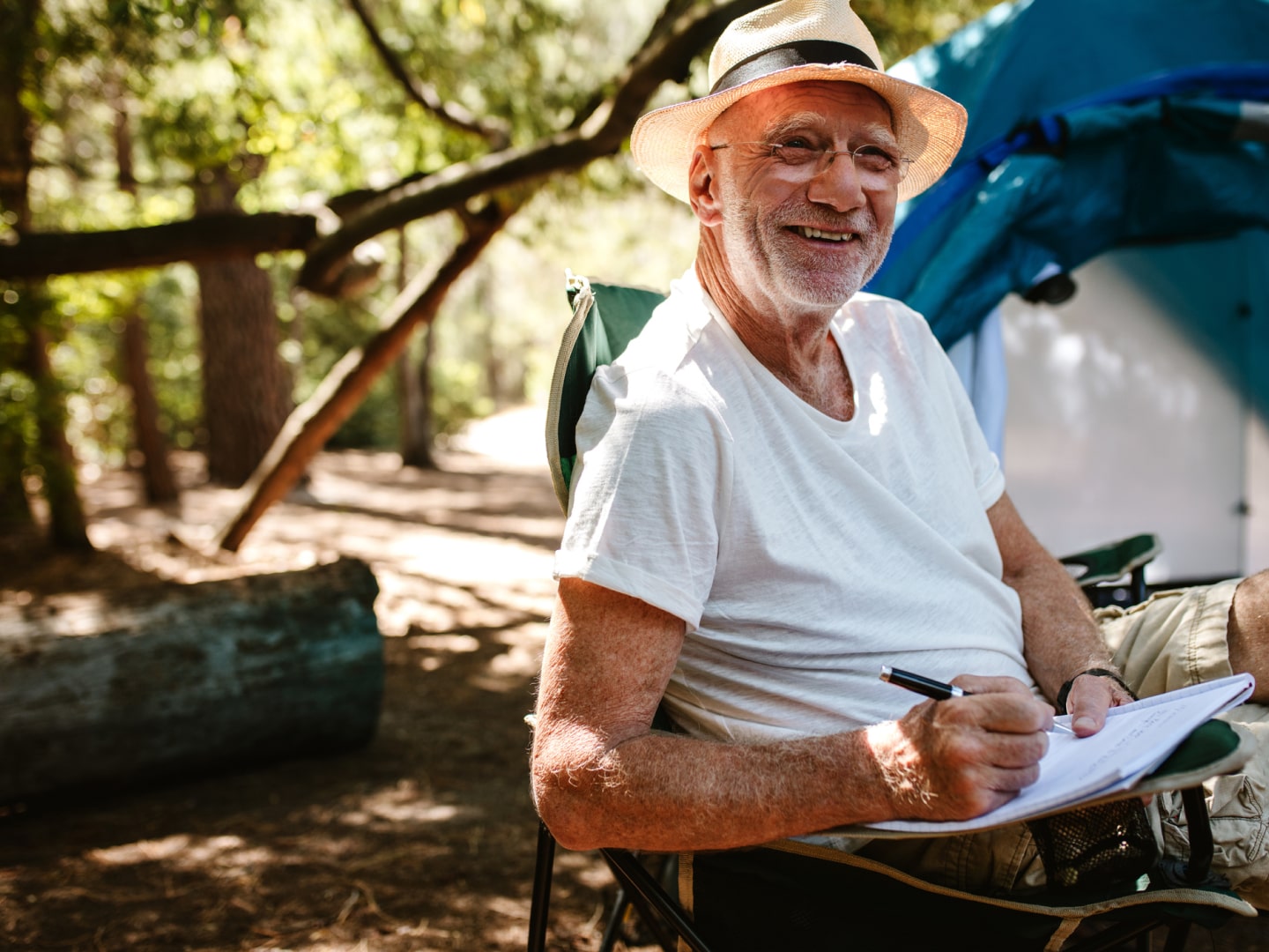 Happy senior man sitting on a camping chair in front of tent in the bush