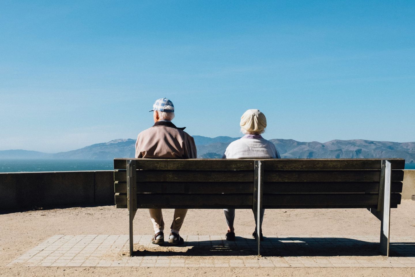 Older retired couple sitting on a bench overlooking the sea