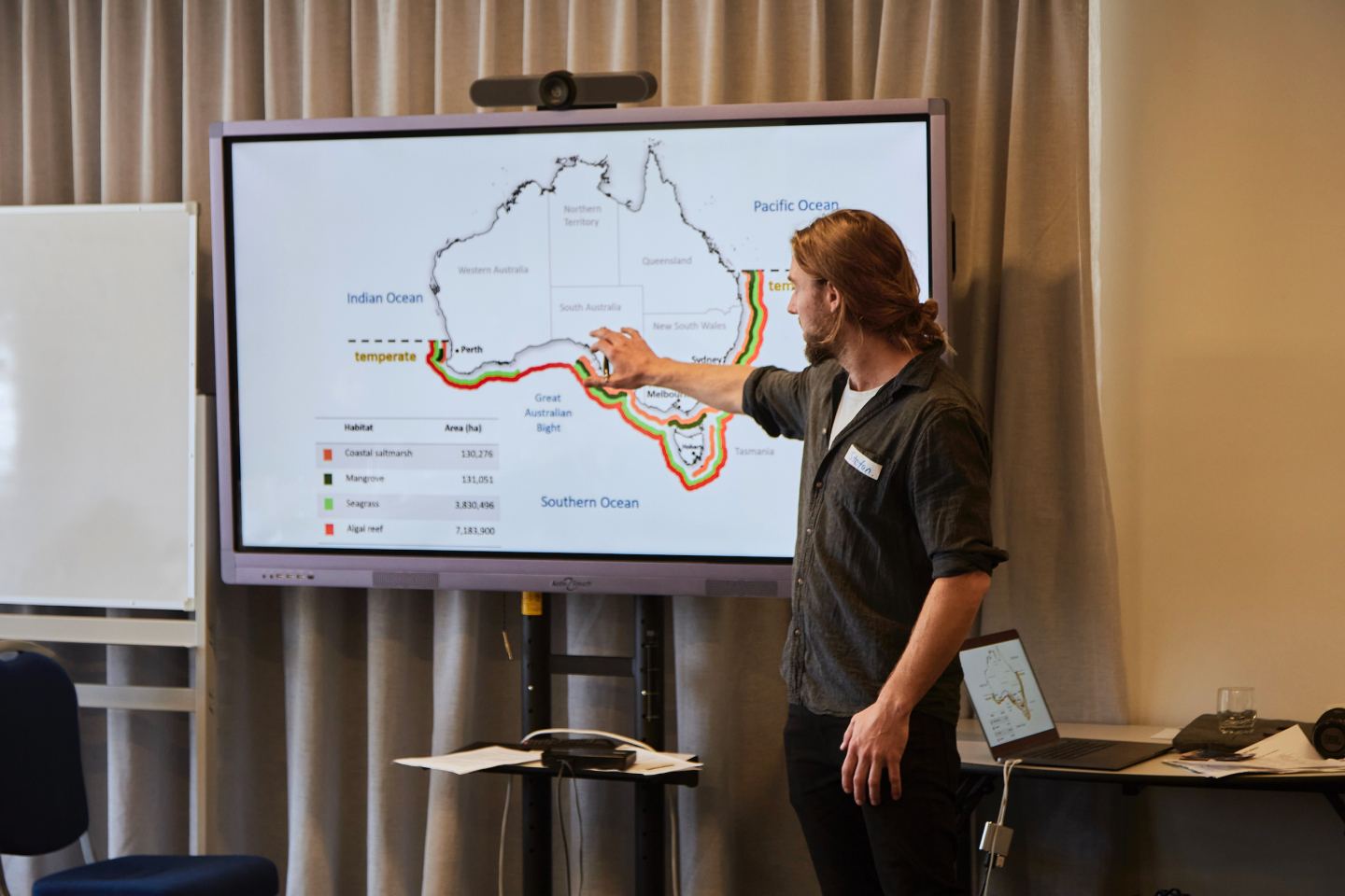 Man pointing out coastal reef features on a projected chart to a room of people